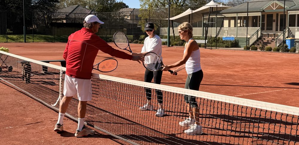 A coach working with two adult players at the net on the clay court