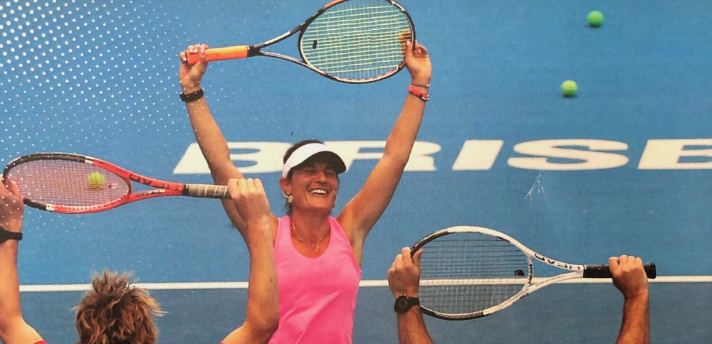 A smiling player with arms and racquet raised, surrounded by others holding racquets up