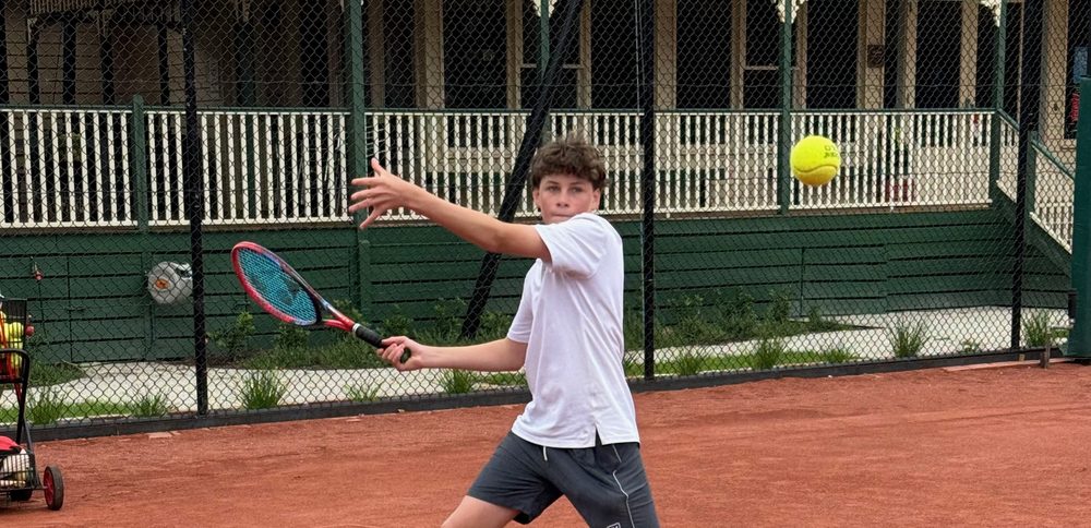 A junior player hitting a forehand on the clay court in front of the ECTC clubhouse