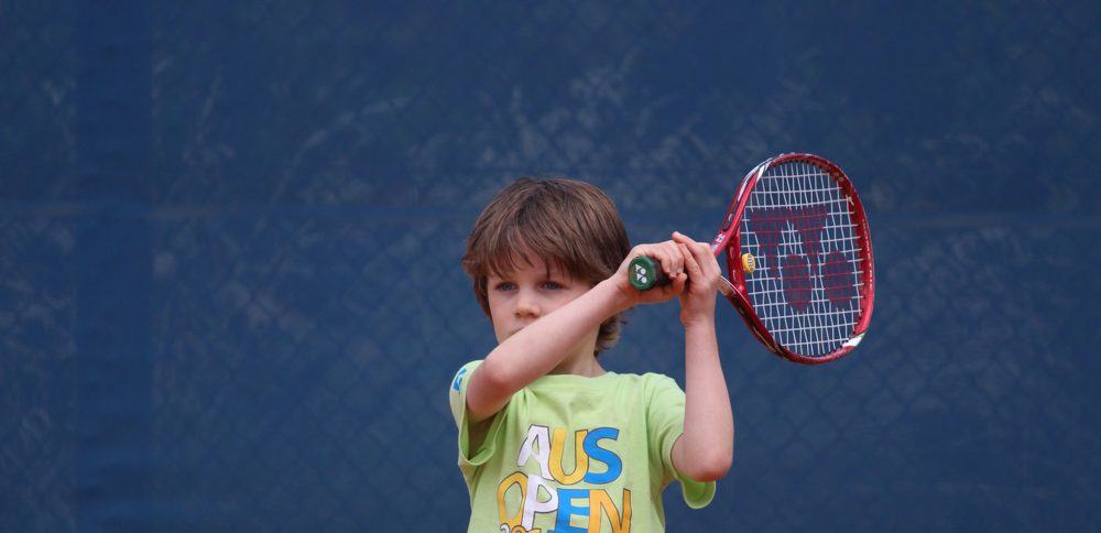 A young player in an Australian Open t-shirt hitting a two-handed backhand
