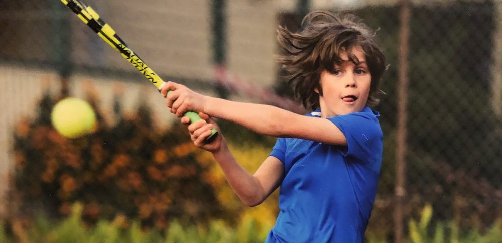 A junior player following through on a powerful two-handed backhand