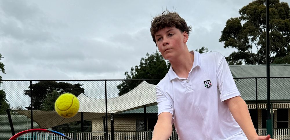 A teenage player reaching for a forehand volley at the net