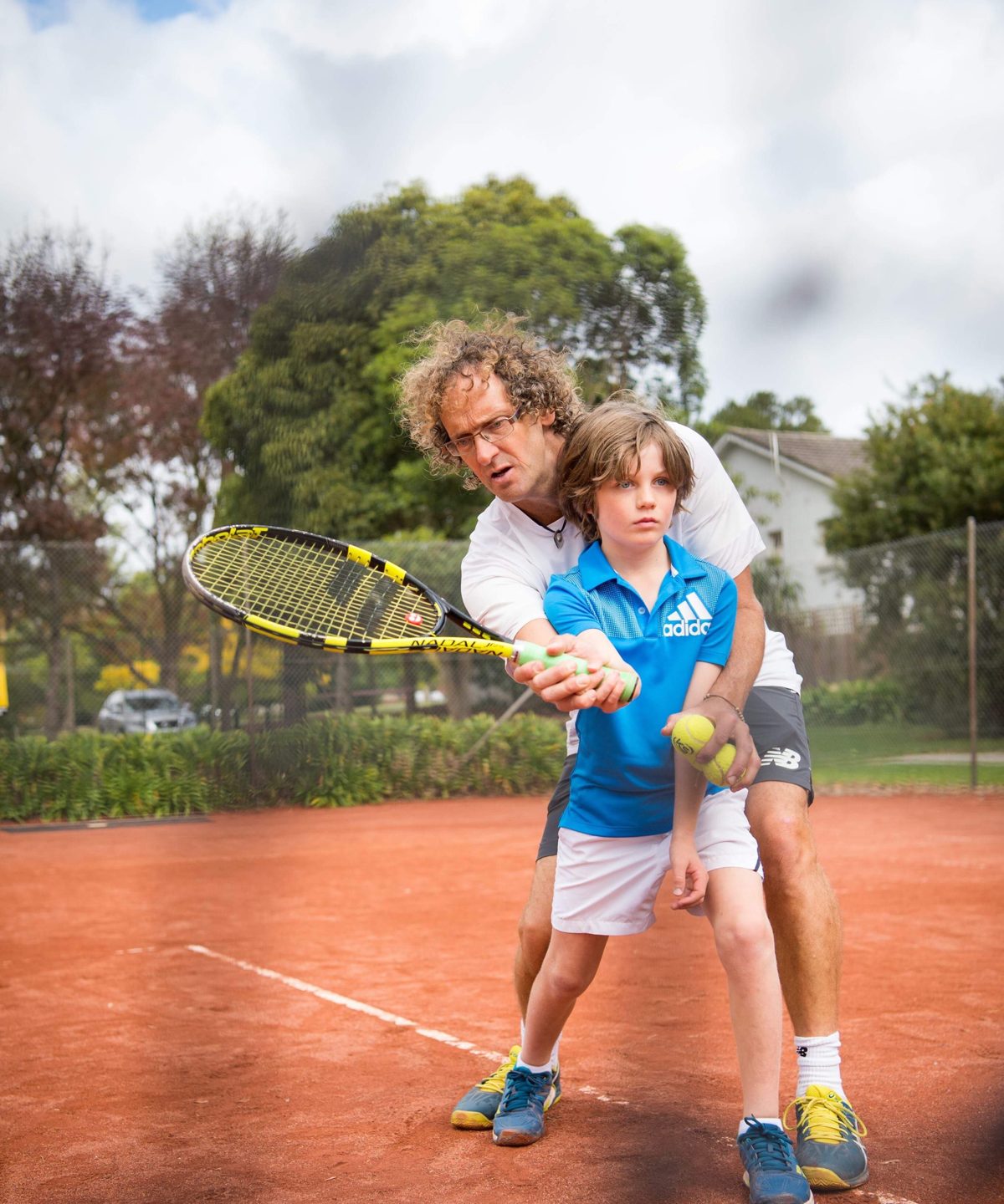 Head coach David Close guiding a young player through a forehand on the clay court