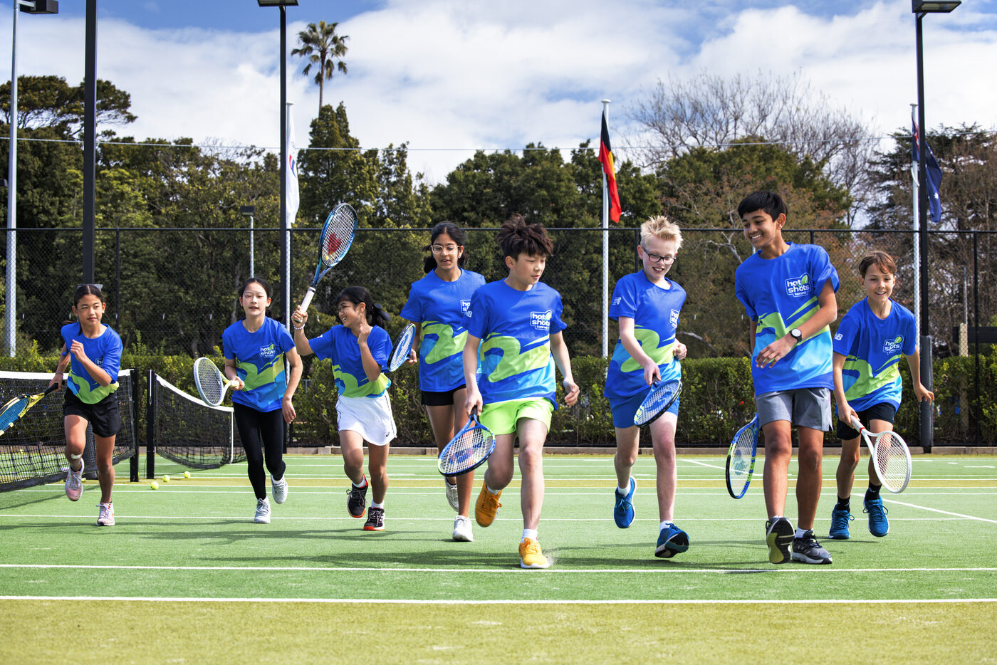 A group of Green stage Hot Shots Tennis players running onto court with their racquets